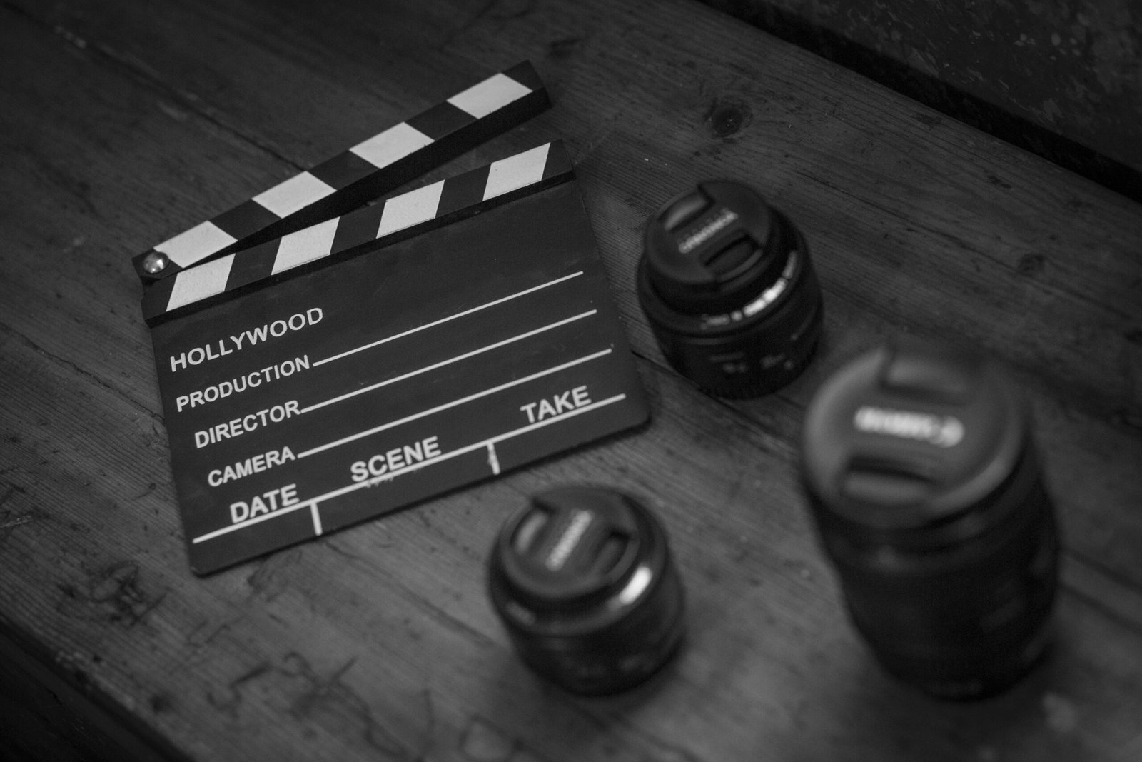 Monochrome image featuring a clapperboard and camera lenses on a wooden table.